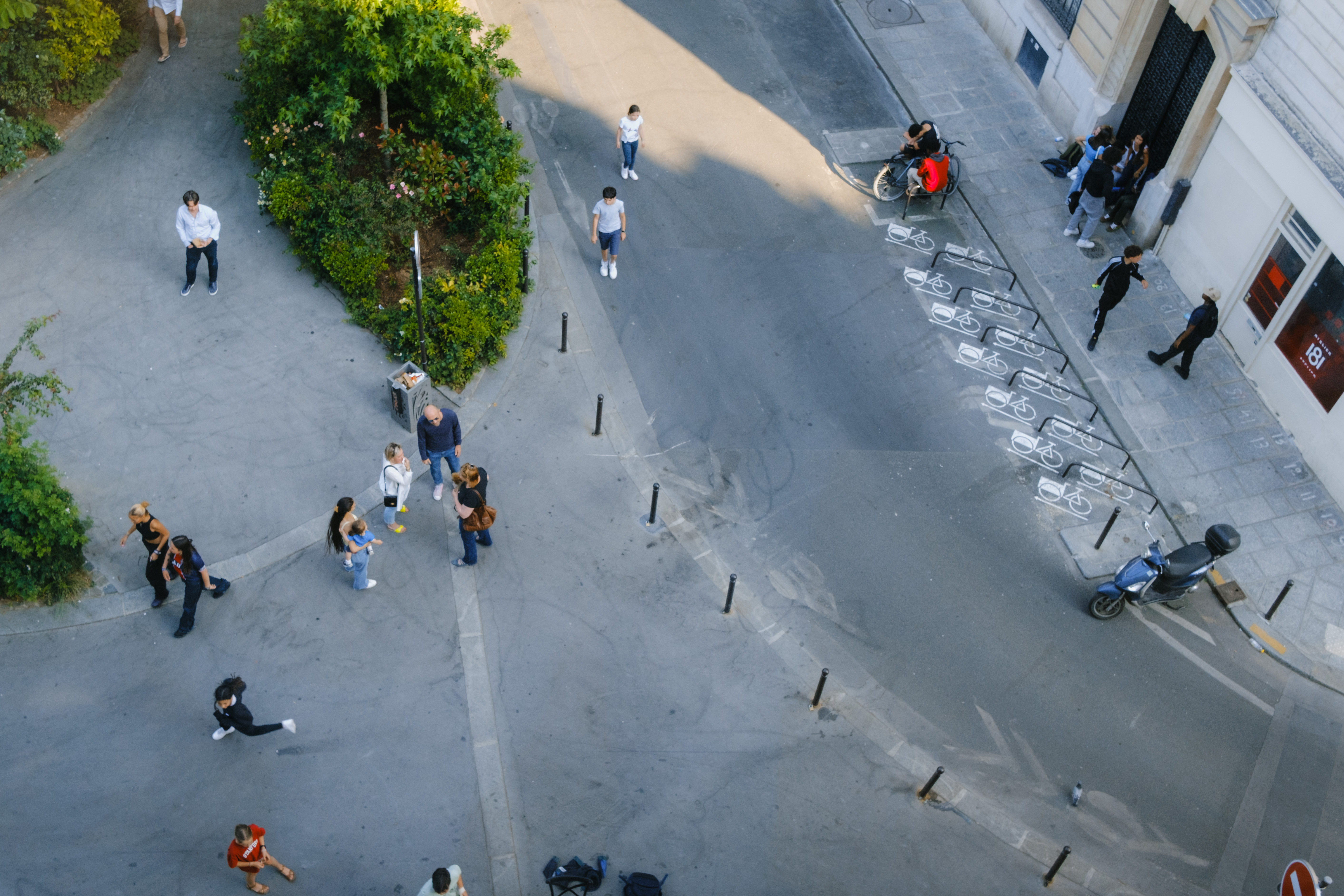 Photo from overhead of people chatting in the street near a park.